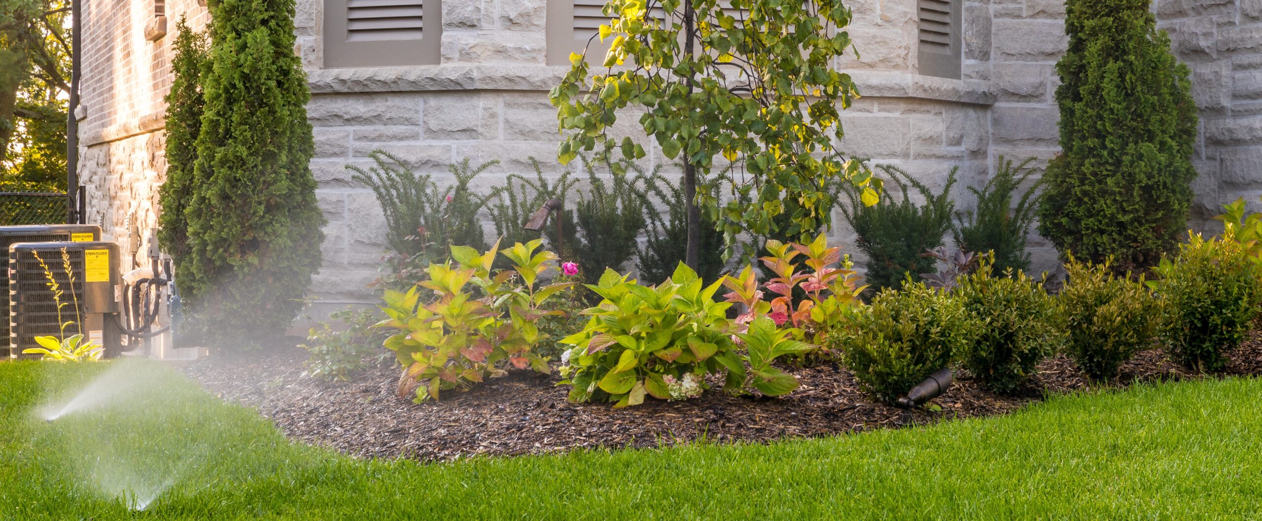 Lawn sprinklers spraying water into a garden outside of a house.